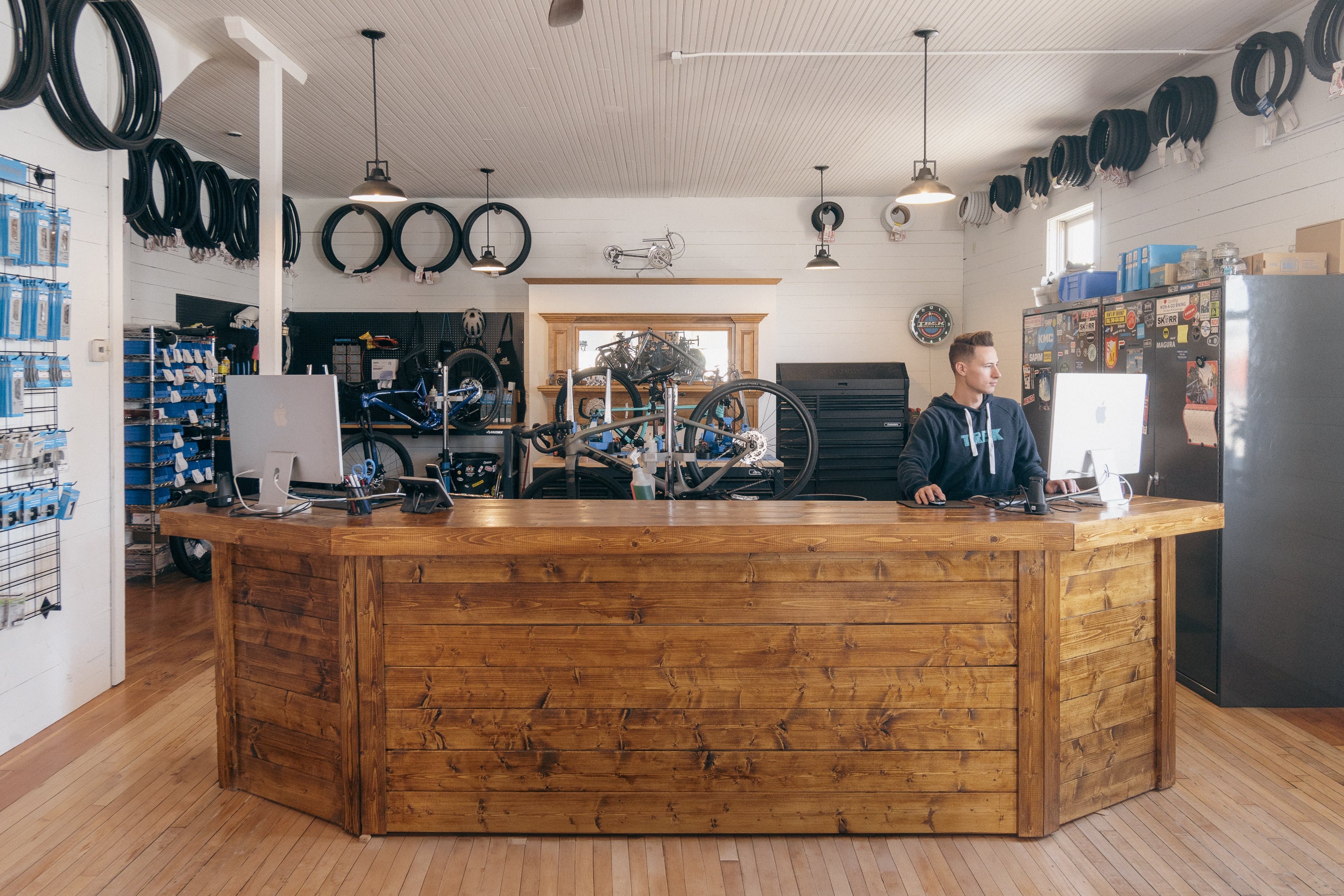 Person behind a wooden counter in a bike shop with tires on the wall.