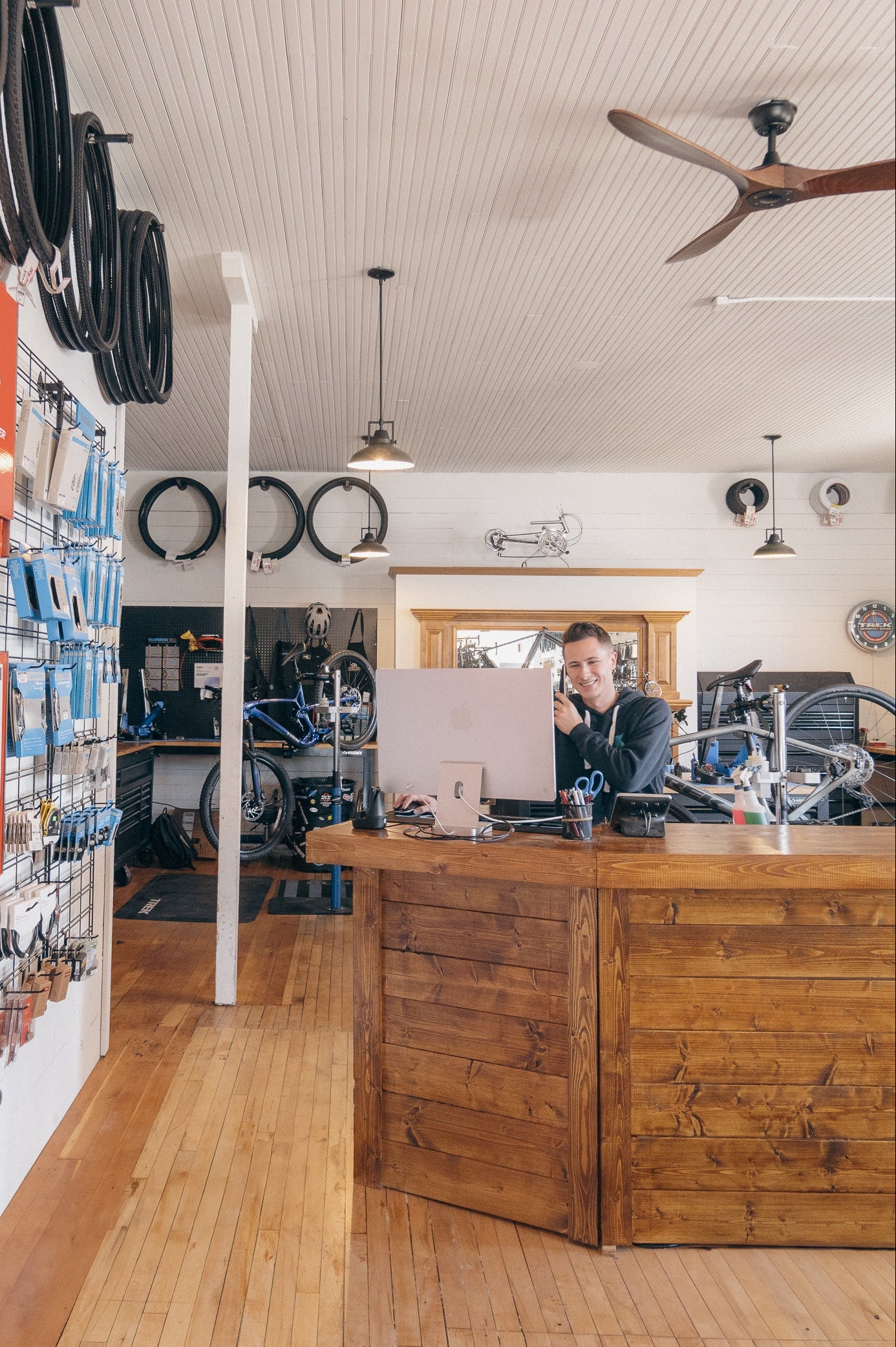 Person behind a counter in a store with wooden floors and ceiling fans.